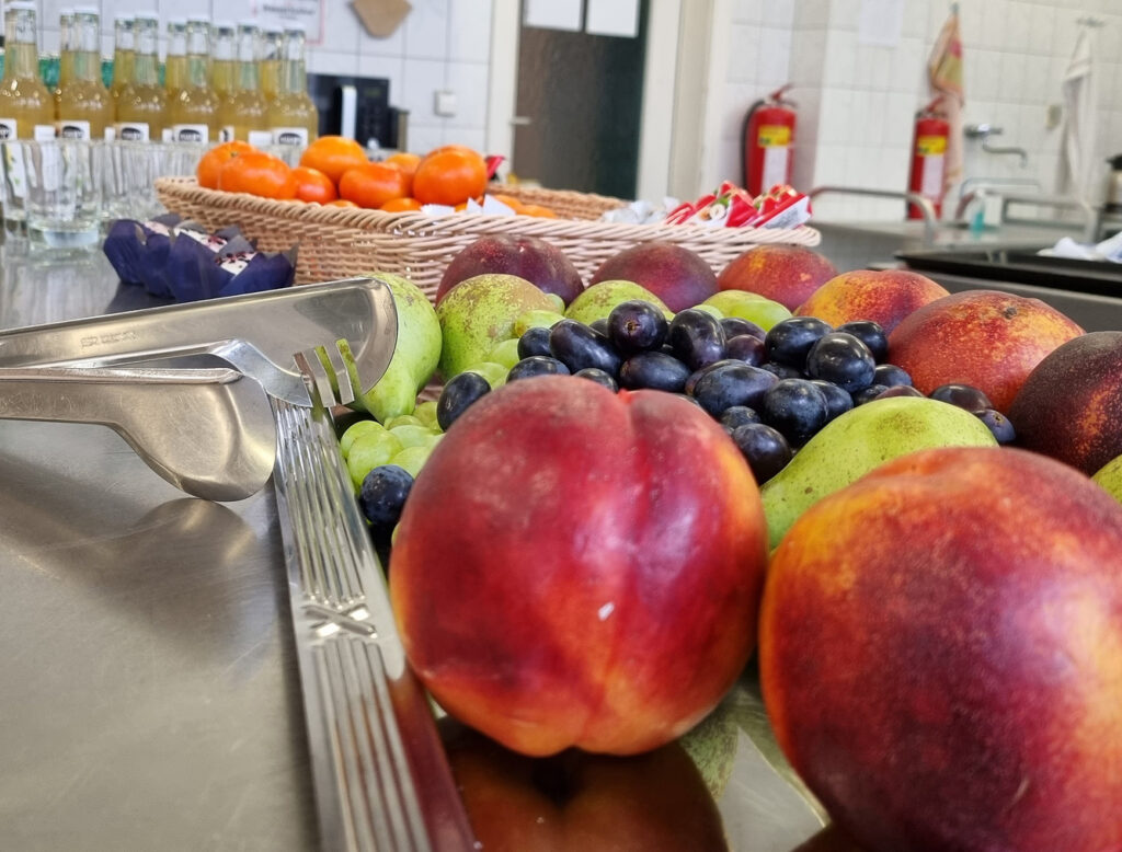 Früchte, Pfirsiche, Trauben usw. im Vordergrund, hinten Getränkeflaschen