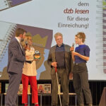 Auf der Bühne stehend: rechts mit Mikrofon Antje Mönnig, links von ihr Thomas Kahlisch und die Moderatorin und ganz links der Moderator