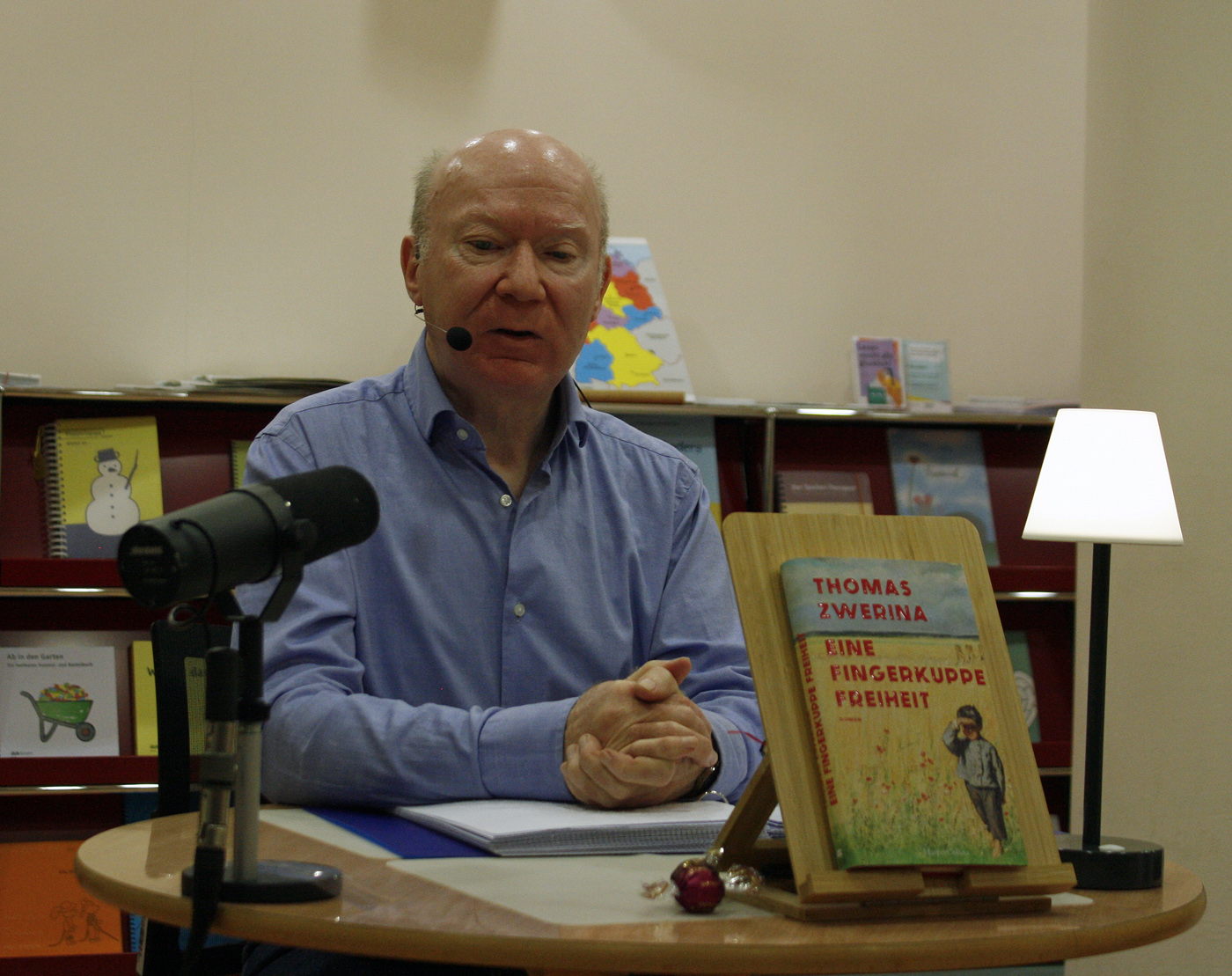 Der Autor des Buches "Eine Fingerkuppe Freiheit" Thomas Zwerina sitzt vor einem runden Tisch, auf dem ein Mikro, sein Buch und eine Leselampe steht.