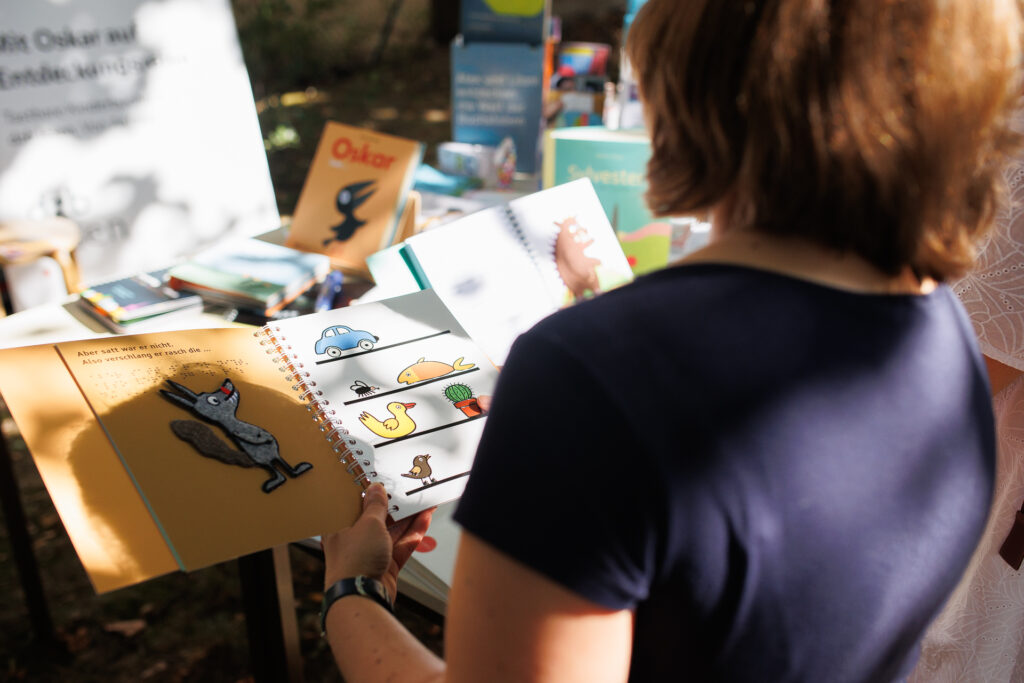 Eine Person mit dem Rücken zum Betrachter hält ein taktiles Kinderbuch in der Hand