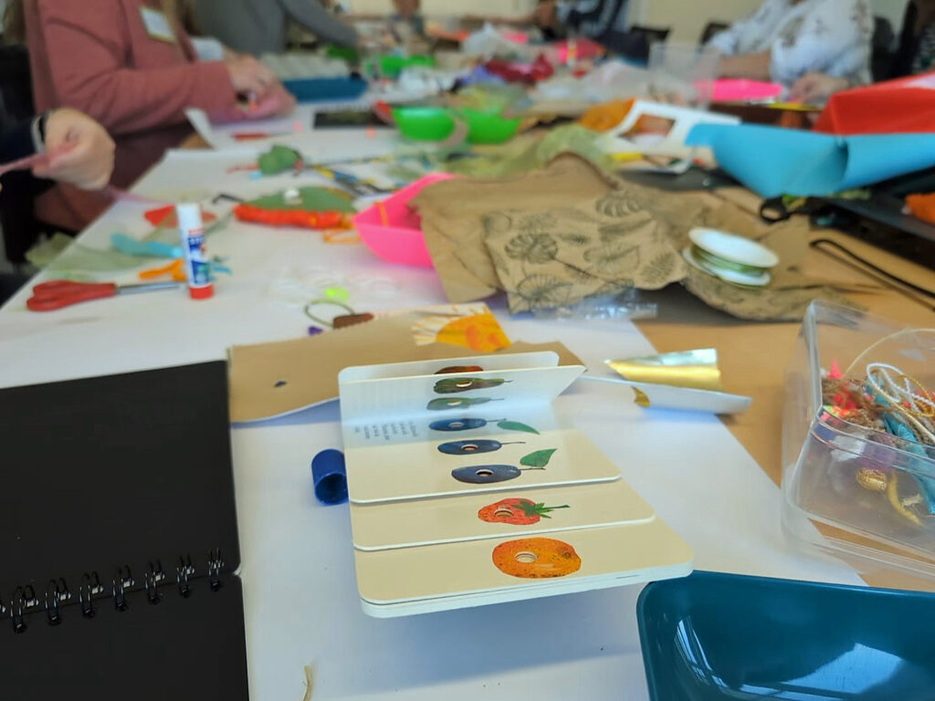 Ein Tisch mit vielen Bastelmaterialien, im Vordergrund ein Kinderbuch.