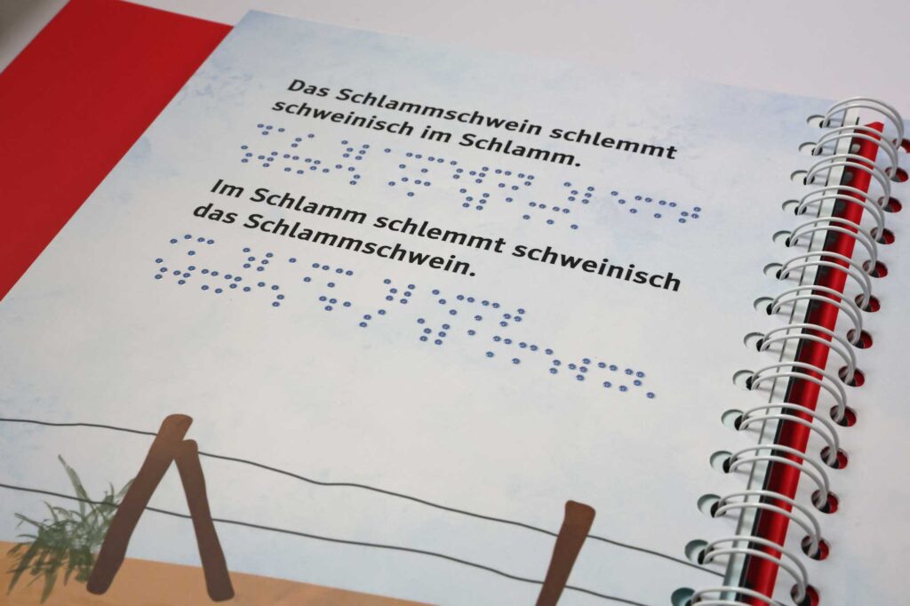 Ein aufgeschlagenes Ringbuch mit Text in Braille- und Großschrift auf der Seite.